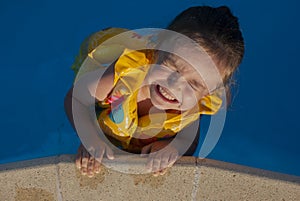 The little girl laughs and holds onto the side of the pool.