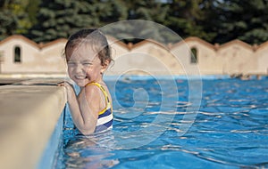 The little girl laughs and holds onto the side of the pool.