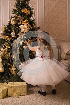 A little girl in a lavish dress dresses up a Christmas tree