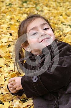 Little girl laying back over yellow leaves