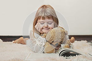 Little girl laying on the floor, reading book with her teddy bear, Christmas background