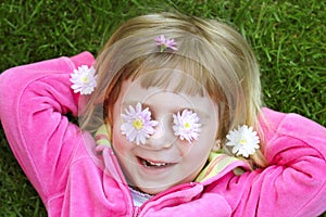 Little girl laying grass daisiy flowers in eyes