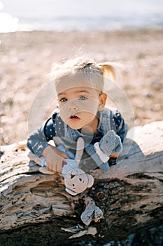 Little girl leaned her stomach against a snag with soft toys in her hands