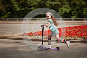 Little girl learn to ride scooter in a park on sunny summer day.