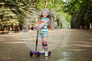 Little girl learn to ride scooter in a park on sunny summer day.