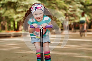 Little girl learn to ride scooter in a park on sunny summer day.