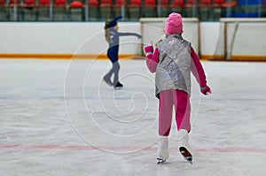 Little girl learning to ice skate. Figure skating school. Young figure skater practicing at indoor skating rink.