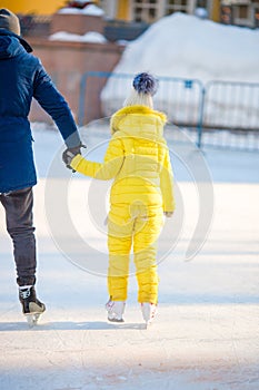 Little girl learning to skate with her father on ice-rink outdoors