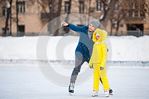 Little girl learning to skate with her father on ice-rink outdoors