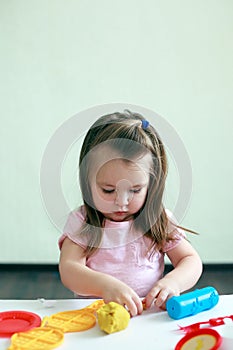 Little girl is learning to use colorful play dough indoor, concept of daycare activity