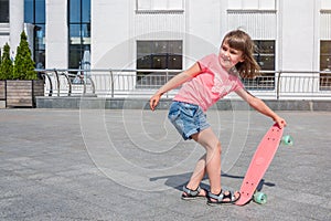 Little girl learns to skateboard on a sunny day outdoors. Lifestyle