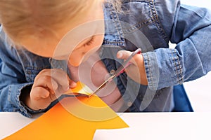 Little girl left-handed cutting construction paper at table