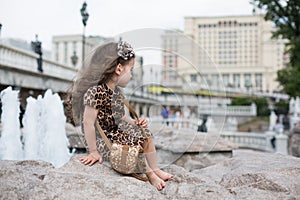 Little girl in a leopard dress sitting on a rock