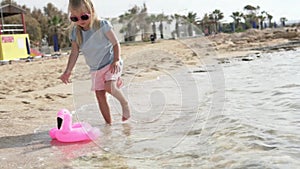 Little girl lets a toy pink flamingo swim in the sea.