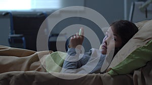 Little girl lie in the bed in the hospital, play with phone