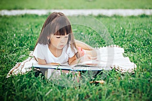 Little girl lie on grass and reading book