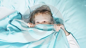 Little girl lies on a bed blue linens the top view hid under a blanket for fear