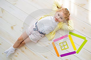 Little girl lies on the floor next to a house of colored paper