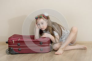 little girl lies leaning on a suitcase and is sad, the concept of vain dreams, no travel, frustration, want to travel