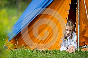 A little girl lies in an orange and blue tent on green grass