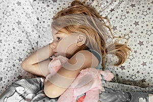 A little girl lies under a blanket with a toy dog getting ready for bed