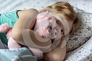 A little girl lies under a blanket with a toy dog getting ready for bed