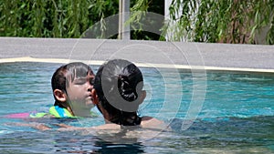 Little girl in a life jacket is afraid to swim in the deep pool. Mother teaching daughter to practice swimming in the pool. Happy