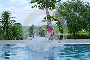 Little girl in a life vest jumps into an outdoor swimming pool. Cute little girl playing in the pool on a sunny day. Summer