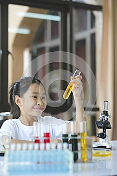 Little girl in lifting and looking at substance in tube in chemistry science class.