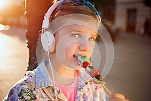 Little girl listening music and eating fruit lollipop,beauti