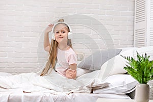 Little girl listening to the music with the headphones on bed.