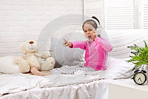 Little girl listening to the music with the headphones on bed.