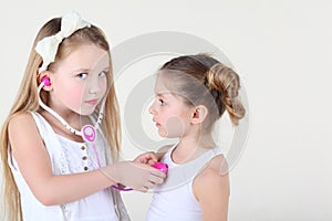 Little girl listens heartbeat of another girl by toy phonendoscope