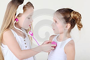 Little girl listens heartbeat of another girl by toy phonendoscope photo