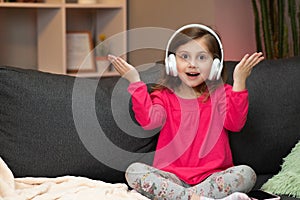 Little Girl Listens To Music On Wireless Headphones. Funny Little Girl Dancing, Singing And Moving To Rhythm. Kid