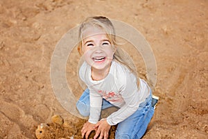 Little girl little girl sitting on the sand on the beach and grins, playing with the sand in the summer