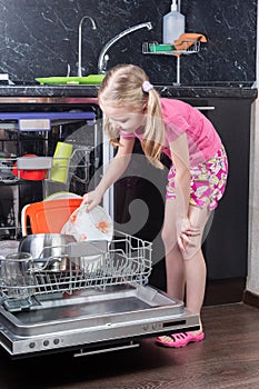 Little girl is loading dishes in dishwasher