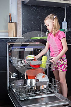 Little girl is loading dishes in dishwasher