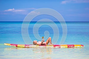 Little girl with lollipop have fun on surfboard in