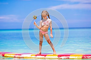 Little girl with lollipop have fun on surfboard in