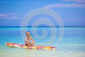 Little girl with lollipop have fun on surfboard in