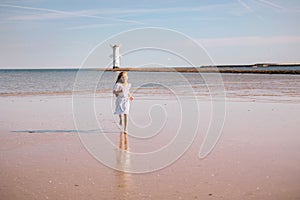 Little girl with lond hair in beautiful dress running on sea beach . Child playing on ocean beach. Sea