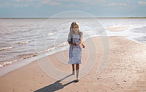Little girl with lond hair in beautiful dress running on sea beach during summer holiday.Child playing on ocean beach. Sea photo