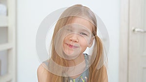 Little girl with long blonde hair blows hair off her face and makes faces