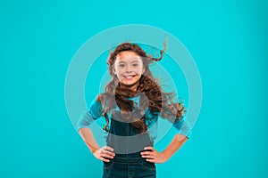 Little girl with long hair. Kid happy cute face with adorable curly hair stand over blue background. Pure beauty. Beauty