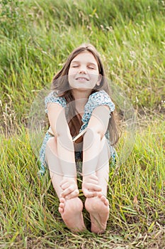 Little girl with long hair sits on the green grass