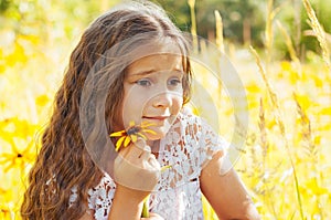 Little girl with long hair in a white dress rejoices in a field with flowers