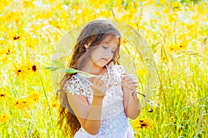 Little girl with long hair in a white dress rejoices in a field with flowers