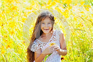 Little girl with long hair in a white dress rejoices in a field with flowers