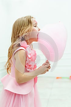 Little girl with long wavy fair hair holding cotton candy with mouth wide opened